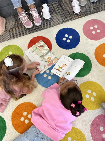 Students lay down on a colorful rug and read books.